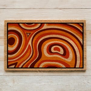 May include: A brown doormat with a geometric pattern of orange, brown, and red swirls. The pattern resembles a retro 70s design.