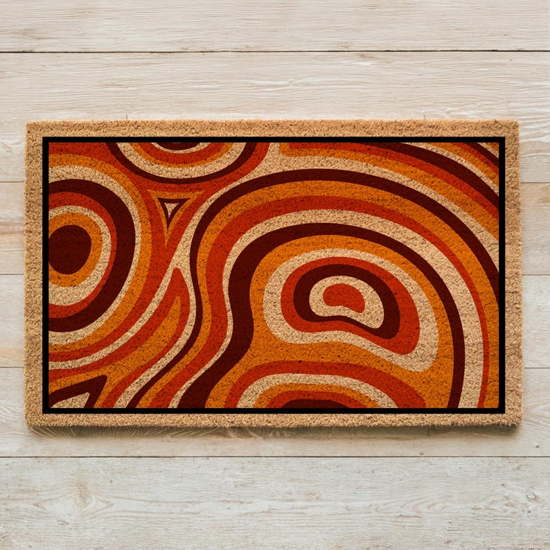 May include: A brown doormat with a geometric pattern of orange, brown, and red swirls. The pattern resembles a retro 70s design.