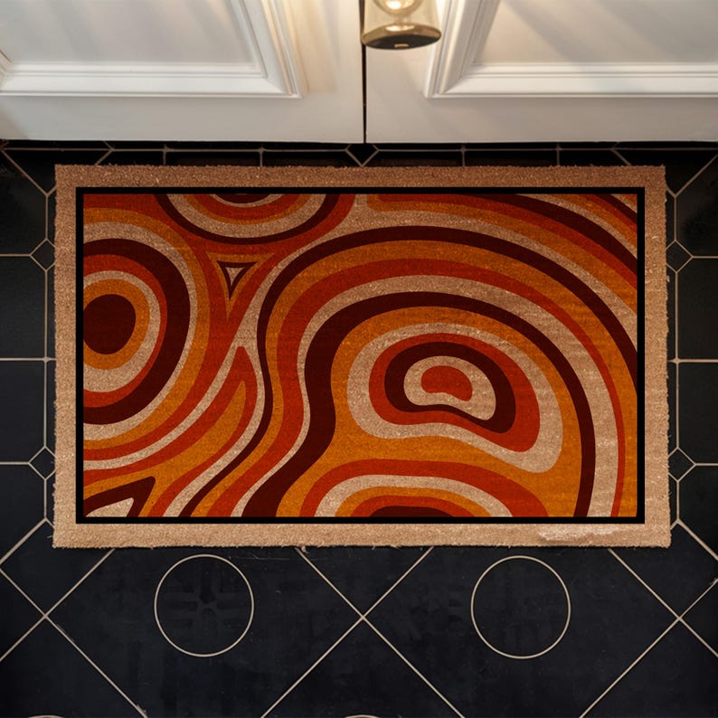 May include: A doormat with a retro-style design featuring swirling orange, brown, and cream coloured lines. The doormat has a brown border.