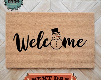 May include: A brown coir doormat with the word "Welcome" in black cursive lettering and a snowman graphic in the center.