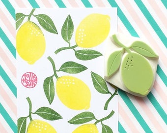 Puede incluir: Una tarjeta blanca con un patrón repetido de limones amarillos con hojas verdes. Un sello de goma verde de un limón con hojas está al lado de la tarjeta. La tarjeta tiene un sello rojo que dice "Talk to the Swirls".