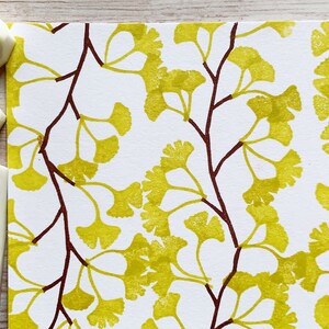 A hand carved rubber stamp set of ginkgo tree design - 3 ginkgo leaves and 1 tree branch, shown with a stamped example in yellow green and brown on white paper. Close-up view of stamped example.