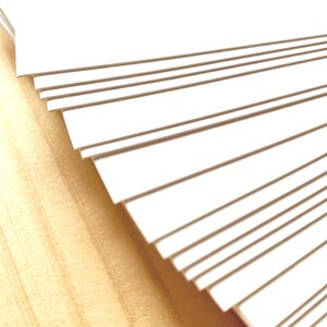May include: A stack of white card stock paper, fanned out to show the edges of each sheet.