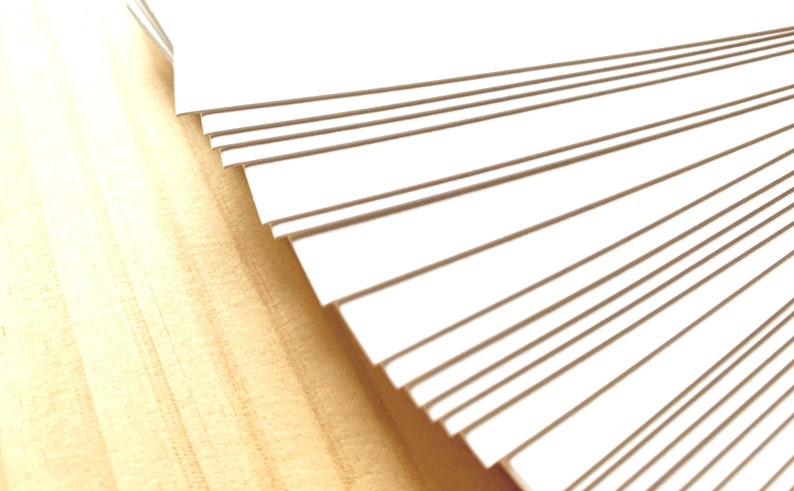 May include: A stack of white card stock paper, fanned out to show the edges of each sheet.