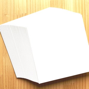 May include: A stack of blank white cards on a wooden surface.