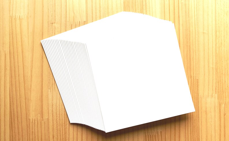 May include: A stack of blank white cards on a wooden surface.
