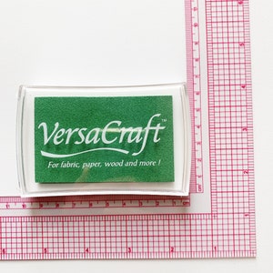 Pode incluir: Uma almofada de tinta verde com um r&oacute;tulo branco que diz "VersaCraft&trade; Para tecido, papel, madeira e muito mais!"