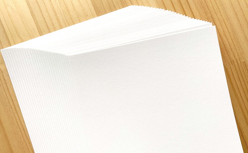 May include: A stack of white paper sheets on a wooden surface.