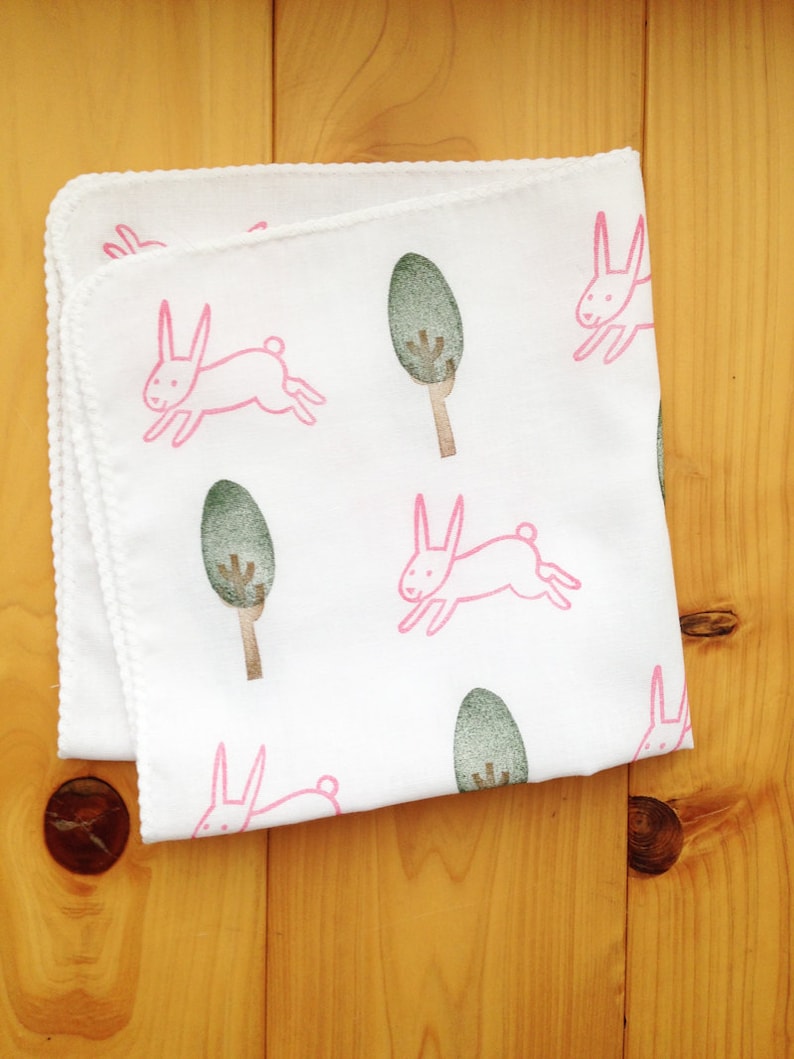 May include: White cotton baby blanket with a pink bunny rabbit and green tree design.