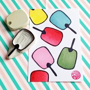 May include: A set of seven colorful rubber stamps shaped like popsicles. The stamps are arranged on a white card with a black outline. The card has a red circle with the text "Make a Wish" in white.