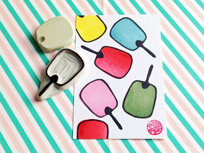 May include: A set of seven colorful rubber stamps shaped like popsicles. The stamps are arranged on a white card with a black outline. The card has a red circle with the text "Make a Wish" in white.
