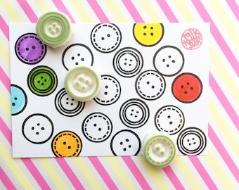 May include: A white card with a black and white button pattern. There are four colorful rubber stamps of buttons on the card. The stamps are green, purple, blue, and red. The card also has a pink stamp with the text "Talk Pretty"
