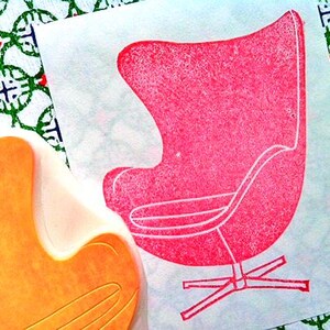 A hand carved rubber stamp of Egg chair, shown with a stamped example in red on white paper.