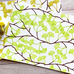 A hand carved rubber stamp set of ginkgo tree design - 3 ginkgo leaves and 1 tree branch, shown with a stamped example in yellow green and brown on white paper.
