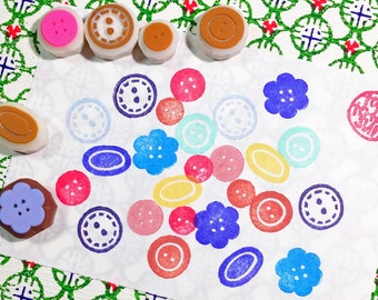 May include: A collection of colorful rubber stamps featuring various button designs. The stamps are arranged on a white surface with a green and white patterned background.