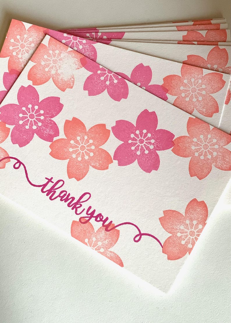A sample image of thank you cards created with hand carved rubber stamps available in the shop. Cherry blossoms and a message "thank you" are stamped in the white card in coral pink and cherry pink.