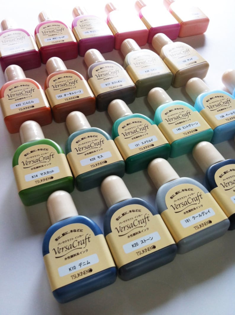 May include: A collection of 18 small bottles of VersaCraft water-based ink in various colors. The bottles are labeled with the color name and the brand name.