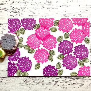 A hand carved rubber stamp set of hydrangea design - flower and leaf, shown with a stamped example in various colored random pattern on white paper.