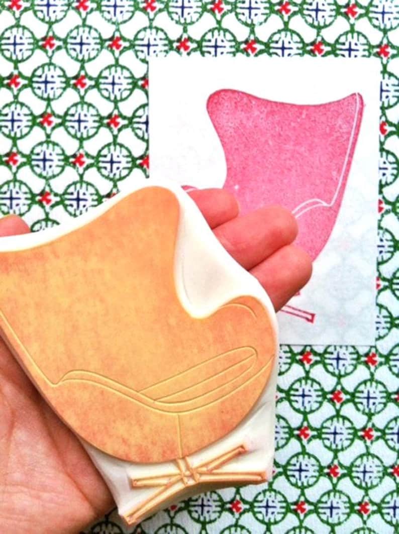 A hand carved rubber stamp of Egg chair, shown with a stamped example in red on white paper. The stamp is held in the hand.