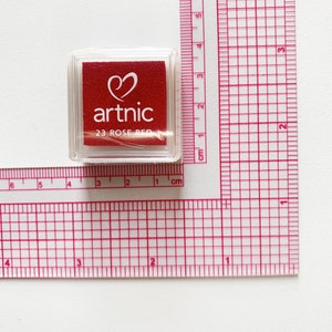 Puede incluir: Una almohadilla de tinta de pl&aacute;stico transparente con una almohadilla de tinta roja en el interior. La almohadilla de tinta tiene un coraz&oacute;n y la palabra "artnic" impresa en ella. La almohadilla de tinta est&aacute; etiquetada como "23 ROSE RED".