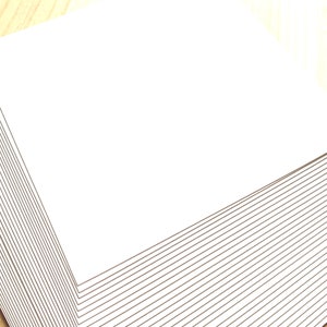 May include: A stack of white paper sheets, neatly aligned and stacked on a wooden surface.