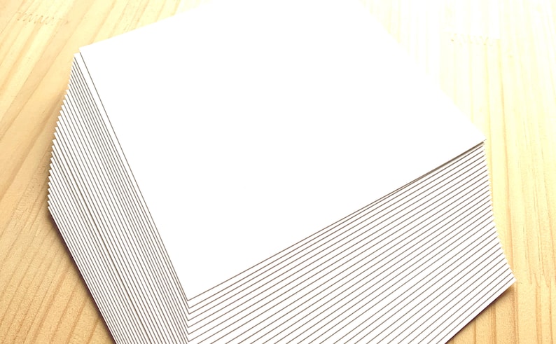 May include: A stack of white paper sheets, neatly aligned and stacked on a wooden surface.
