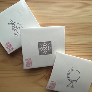 A sample image of packagings for hand carved rubber stamps - wrapped with glassine paper and a stamped example card.