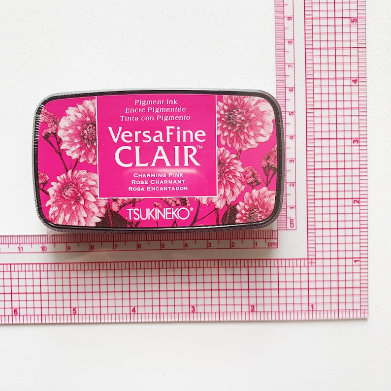 May include: A rectangular ink pad with a pink floral design and the text "VersaFine CLAIR" in white. The ink pad is labeled "Charming Pink" and measures approximately 3 inches by 2 inches.