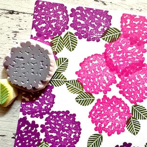 A hand carved rubber stamp set of hydrangea design - flower and leaf, shown with a stamped example in various colored random pattern on white paper.