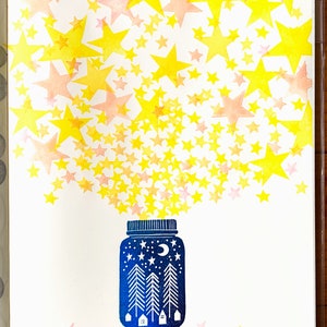 May include: A blue glass jar with a moon and stars design, filled with yellow and pink stars spilling out of the top.