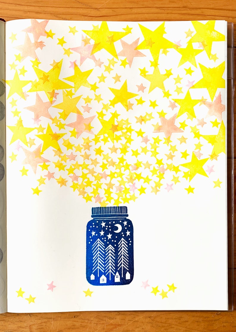 May include: A blue glass jar with a moon and stars design, filled with yellow and pink stars spilling out of the top.