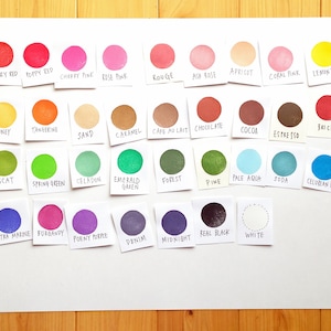 Pode incluir: Uma tabela de 24 amostras de tinta de diferentes cores com o nome de cada cor escrito abaixo. As cores incluem vermelho cereja, vermelho papoula, rosa cereja, rosa claro, vermelho, rosa cinza, damasco, rosa coral, amarelo lim&atilde;o, mel, tangerina, areia, caramelo, caf&eacute; com leite, chocolate, cacau, expresso, tijolo, noz-moscada, verde primavera, celadon, verde esmeralda, floresta, pinho, azul claro, soda, azul celeste, azul ultramar, bord&ocirc;, roxo pe&ocirc;nia, denim, meia-noite, preto verdadeiro, e branco.