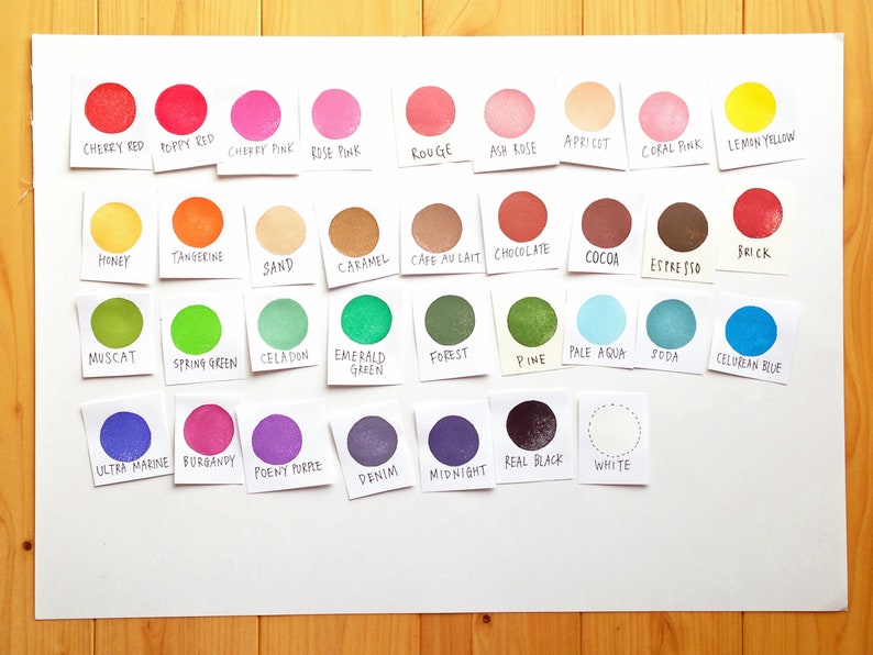 Pode incluir: Uma tabela de 24 amostras de tinta de diferentes cores com o nome de cada cor escrito abaixo. As cores incluem vermelho cereja, vermelho papoula, rosa cereja, rosa claro, vermelho, rosa cinza, damasco, rosa coral, amarelo lim&atilde;o, mel, tangerina, areia, caramelo, caf&eacute; com leite, chocolate, cacau, expresso, tijolo, noz-moscada, verde primavera, celadon, verde esmeralda, floresta, pinho, azul claro, soda, azul celeste, azul ultramar, bord&ocirc;, roxo pe&ocirc;nia, denim, meia-noite, preto verdadeiro, e branco.