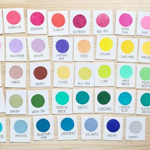 Puede incluir: Una carta de colores con 36 colores de pintura diferentes, cada color est&aacute; etiquetado con su nombre. Los colores est&aacute;n dispuestos en filas y columnas, y la carta est&aacute; sobre una superficie de madera.