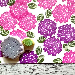 A hand carved rubber stamp set of hydrangea design - flower and leaf, shown with a stamped example in various colored random pattern on white paper.