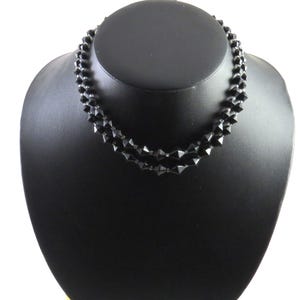 May include: A black necklace made of faceted beads. The necklace is displayed on a black mannequin bust.