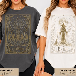May include: Two t-shirts with witch-themed designs. One is a dark gray shirt with a gold illustration of witches and the text "THE COVEN". The other is an ivory shirt with a gold illustration of a witch and the text "THE BRIDE".