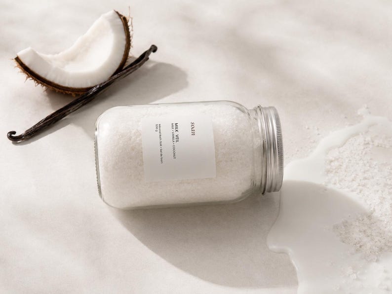 Jar of pale creamy Milk Veil bath soak made with mineral salts, milk powder, coconut, and vanilla fragrance
