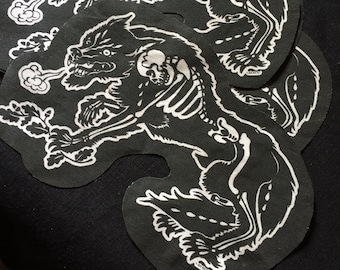 Puede incluir: Parches en blanco y negro con un diseño de lobo esquelético. La caja torácica y el cráneo del lobo son visibles. El lobo sostiene una ramita con hojas. Los parches tienen una forma única y están hechos de tela.