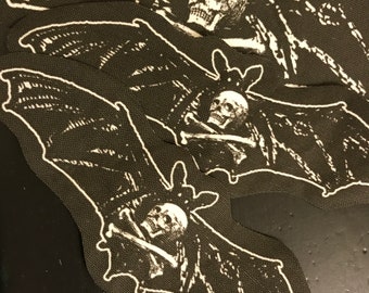 Puede incluir: Tres parches de tela negra con murciélagos y calaveras bordadas en blanco. Cada murciélago tiene una calavera con huesos cruzados en la boca.