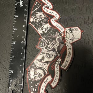 May include: A black and red sticker in the shape of a bat, featuring illustrations of vampires and the phrases "Sleep All Day, Party All Night, Never Grow Old, It's Fun to Be a Vampire, Never Die." The sticker measures approximately 18 cm in length.