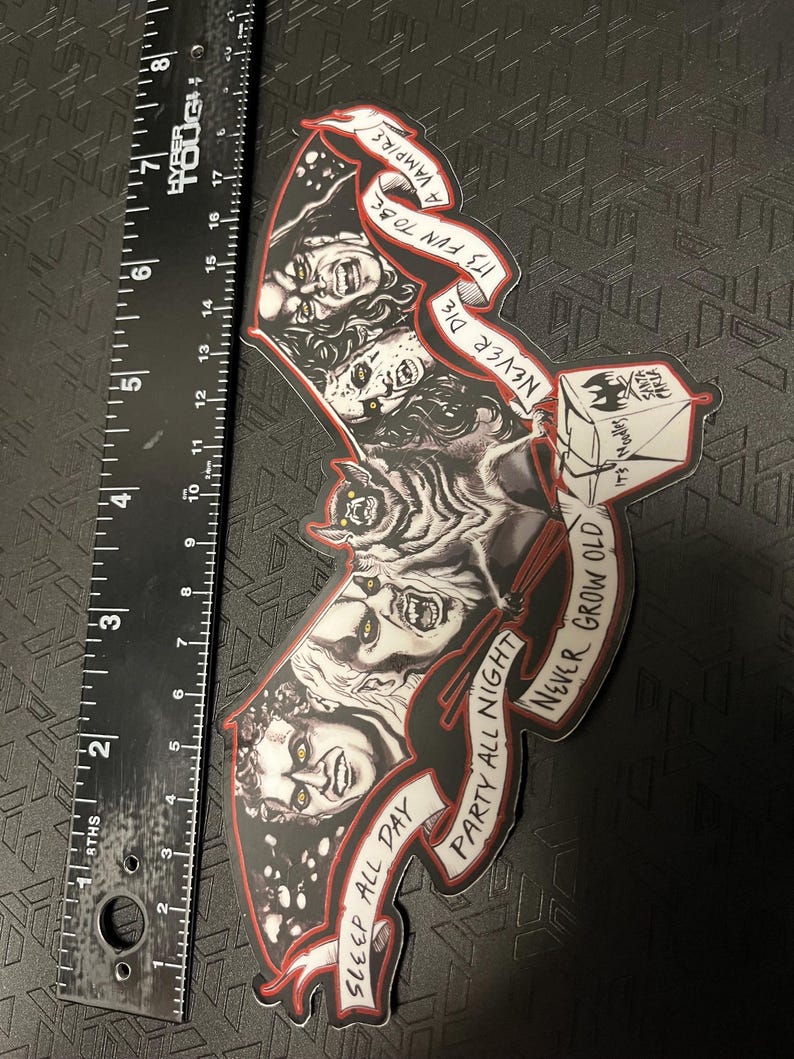 May include: A black and red sticker in the shape of a bat, featuring illustrations of vampires and the phrases "Sleep All Day, Party All Night, Never Grow Old, It's Fun to Be a Vampire, Never Die." The sticker measures approximately 18 cm in length.