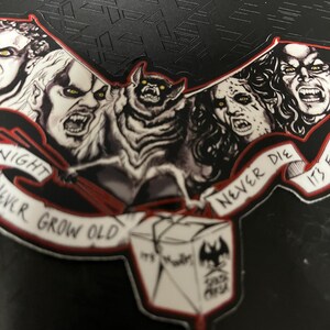 May include: A black and red sticker with illustrations of vampires and a bat. The sticker has the text "Night Never Grow Old" and "Never Die". A box with the text "It's Murder" and a bat logo is also featured.