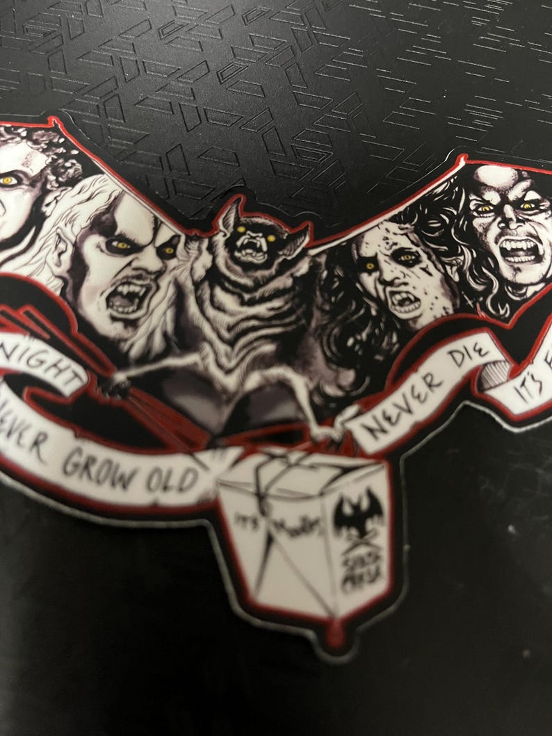 May include: A black and red sticker with illustrations of vampires and a bat. The sticker has the text "Night Never Grow Old" and "Never Die". A box with the text "It's Murder" and a bat logo is also featured.