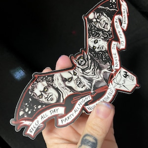 May include: A bat-shaped sticker with a black and red design featuring vampire illustrations and text. The text includes phrases like "Sleep All Day," "Party All Night," and "It's Fun to Be a Vampire."