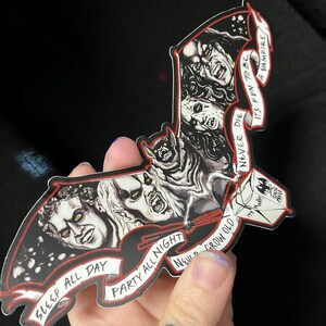 May include: A black and red bat-shaped sticker with vampire illustrations and the phrases "Sleep All Day", "Party All Night", and "Never Grow Old". The sticker also includes the text "It's Fun To Be A Vampire".