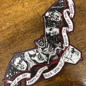 May include: A bat-shaped sticker with vampire imagery in black and white. The design includes the phrases "Sleep All Day", "Party All Night", and "Never Grow Old". The sticker also features the text "It's Fun to be a Vampire".