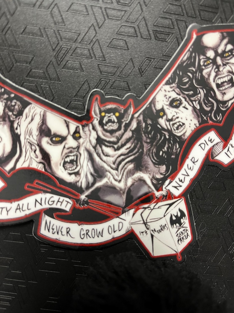 May include: A bat-shaped sticker with a bat holding chopsticks and several vampire faces. The sticker has the text "Party All Night, Never Grow Old" and a Santa Carla Noodles logo.