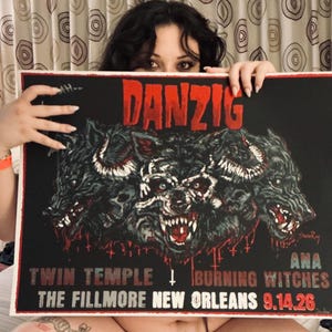May include: A rectangular concert poster featuring the band name DANZIG in red text at the top. The central graphic depicts a three-headed wolf with skull-like features. Below, the text reads TWIN TEMPLE, BURNING WITCHES, THE FILLMORE NEW ORLEANS, 9.14.26.