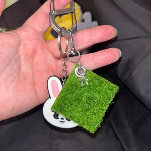 Puede incluir: Un llavero con un conejito blanco con orejas rosas y un cuadrado verde con un dije de estrella. El llavero est&aacute; sujeto a un mosquet&oacute;n y llaveros plateados.
